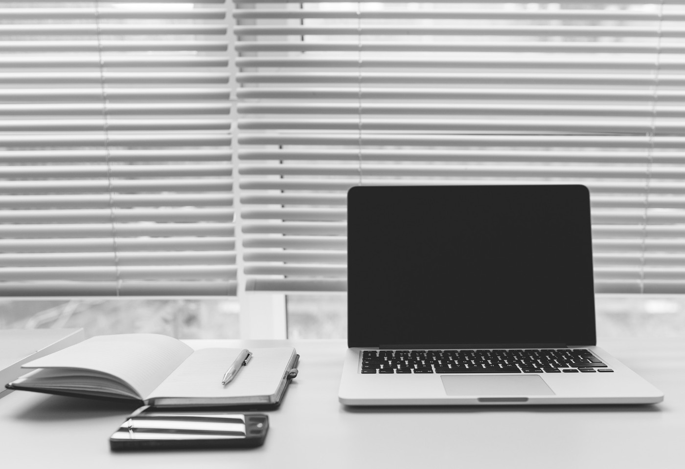 Laptop, phone and notebook next to window with blinds - How to Soundproof Windows Yourself - 6 Ways that Actually Work!