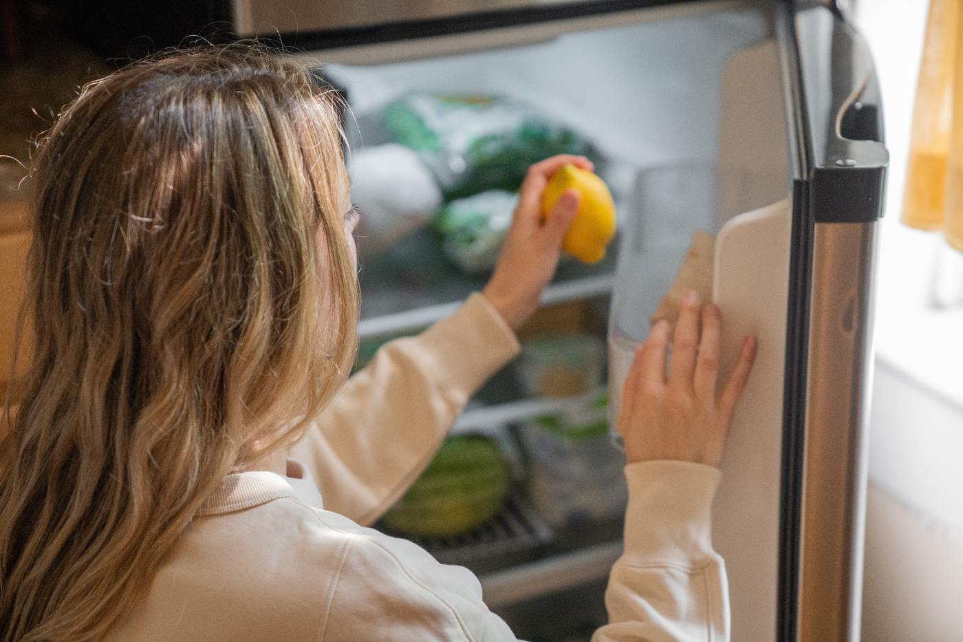 Mujer abriendo el frigorífico y sujetando un limón - Cómo reducir el ruido del frigorífico