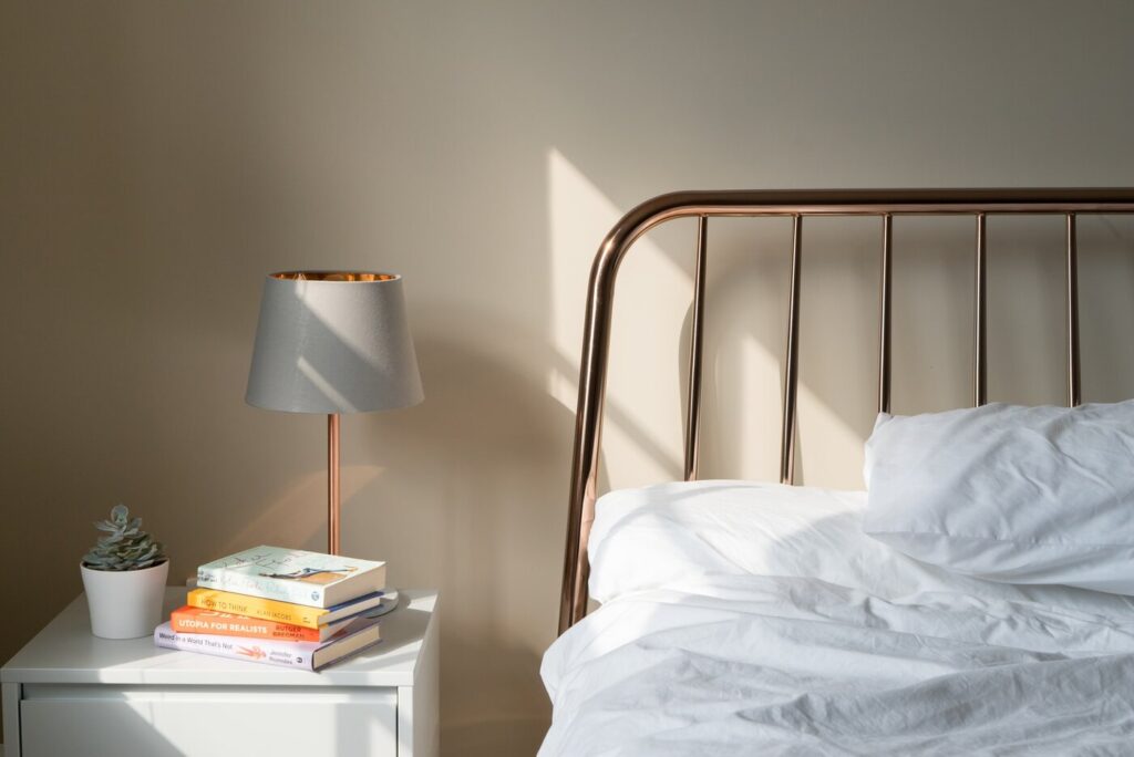Bett und Nachttisch mit Büchern und Lampe - was Sie über die Schallisolierung Ihres Schlafzimmers wissen müssen